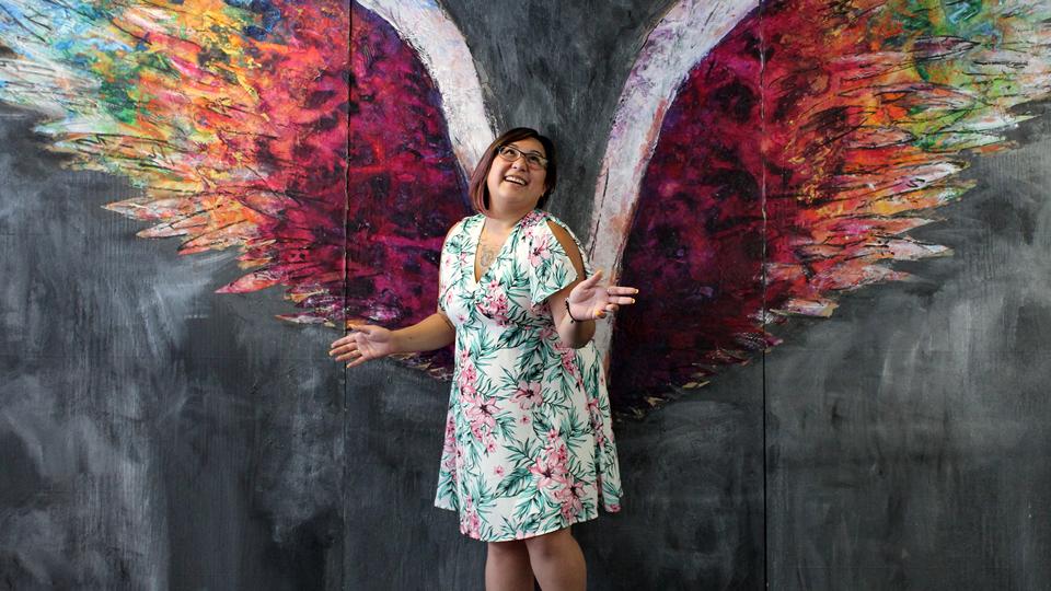  凡妮莎 说睡觉 poses in front of a colorful wall mural of angelic colorful wings.